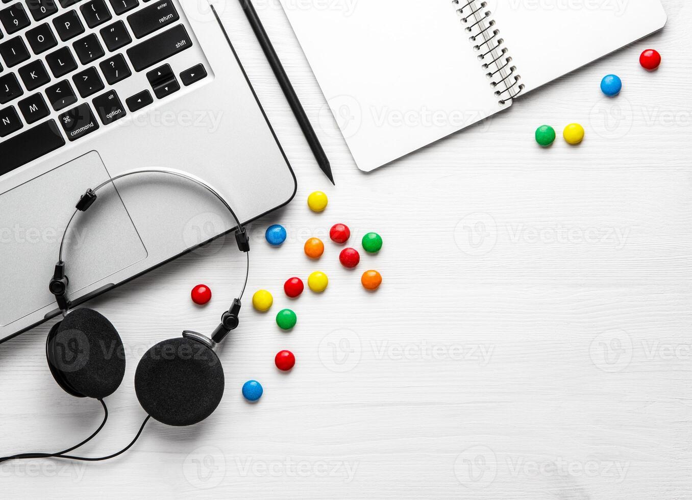 Notebook headphones, laptop and multi-colored sweets on a white background. Flat lay with copy space. photo