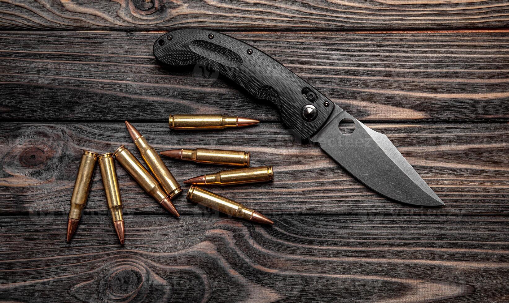 Pocket folding knife and a few rifle cartridges on a wooden back photo