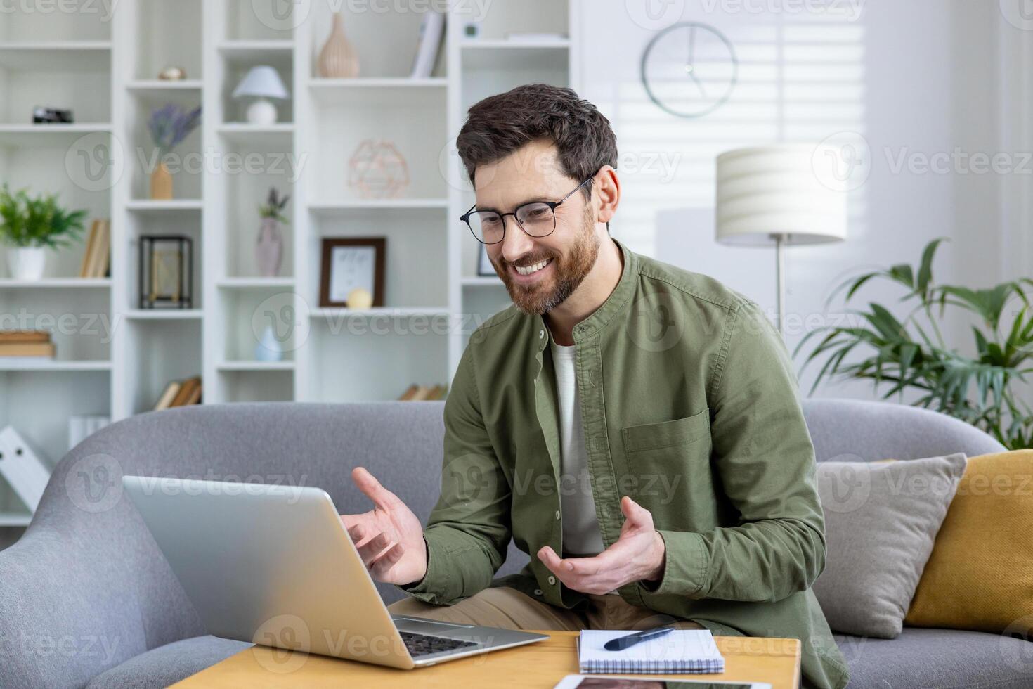 Smiling man talking during a call on his laptop in a bright and modern home office space. photo