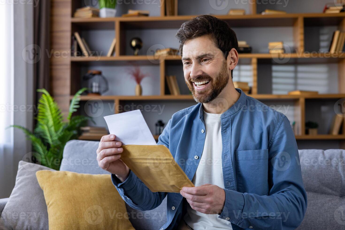 Happy adult male in a casual shirt, enjoying reading a letter while sitting comfortably on a sofa in a cozy living room. photo
