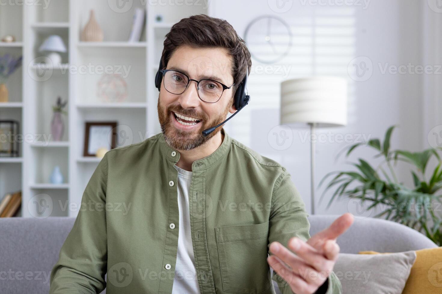 Smiling man wearing a headset and glasses, conducting an online meeting from his modern home office, explaining something enthusiastically. photo