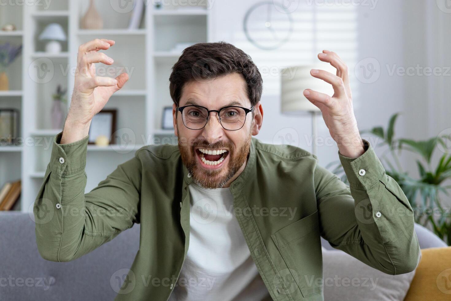 Man in casual outfit with glasses showing frustration and anger in a home setting. Emotions of stress and anxiety clearly visible. photo