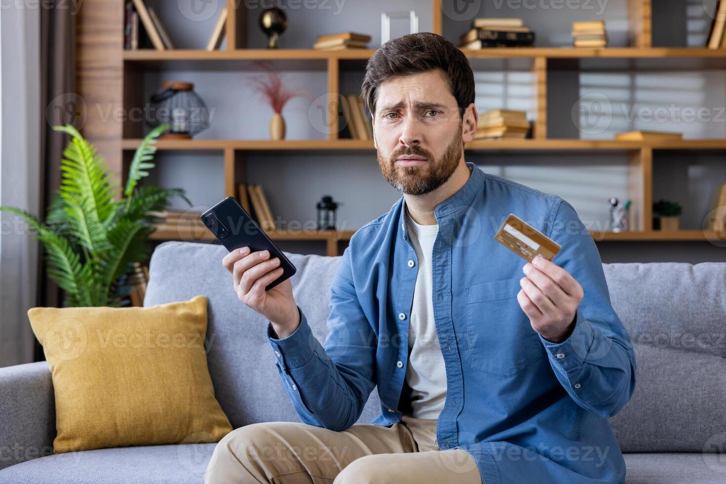 A perplexed adult male with a smart phone and credit card, showing potential online shopping issues or finance management. photo