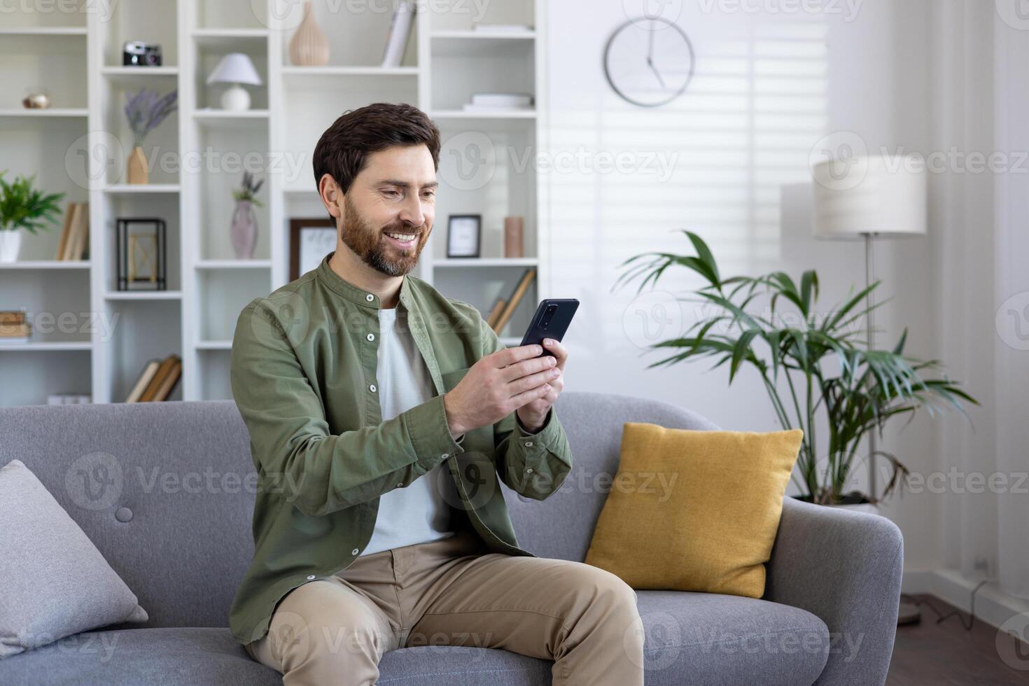 Satisfied mature man sitting on sofa in living room, using app on phone, freelancer holding smartphone, reading and typing text message, browsing social media. photo