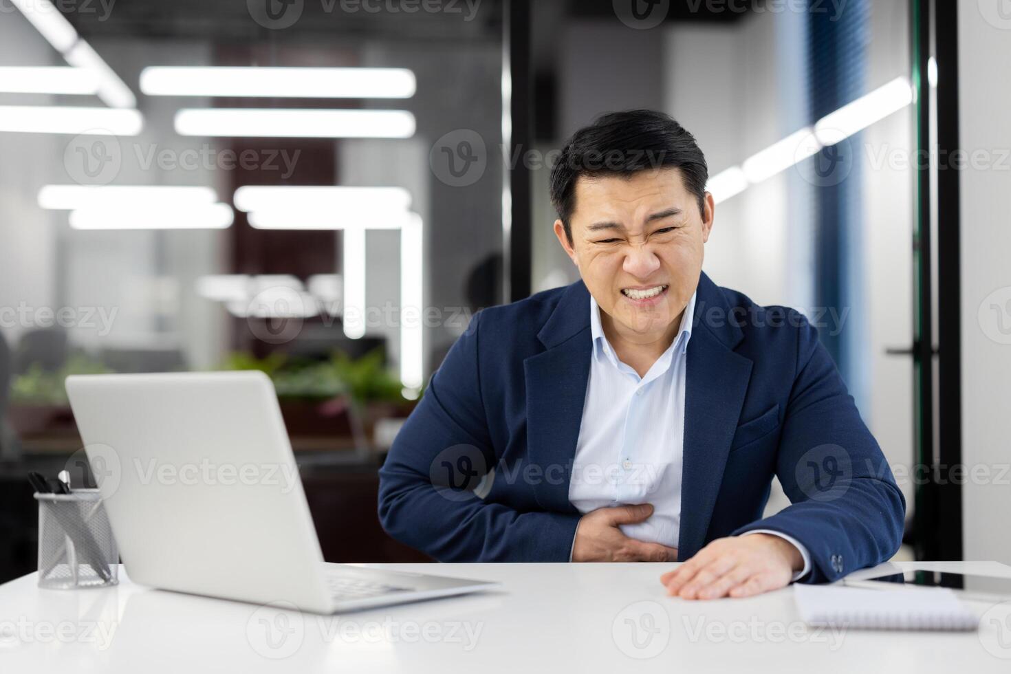 Man has severe stomach pain, nausea and food poisoning, businessman inside office at workplace, worker in business suit working with laptop. photo