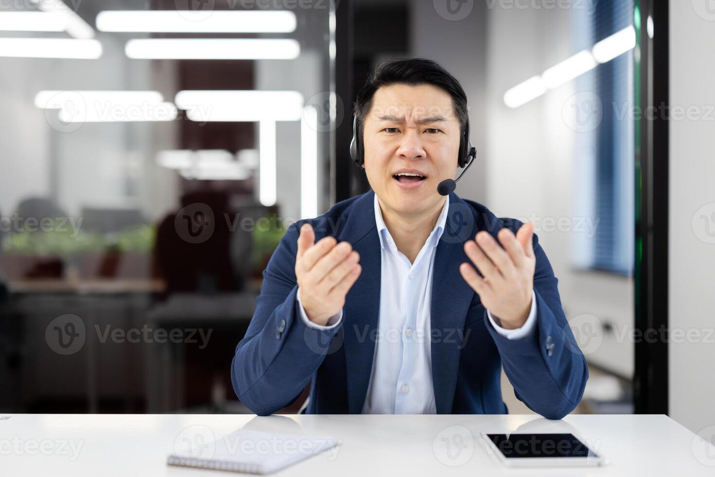 An Asian businessman in a modern office feels frustration during a call. Customer service challenges and technical difficulties depicted. photo