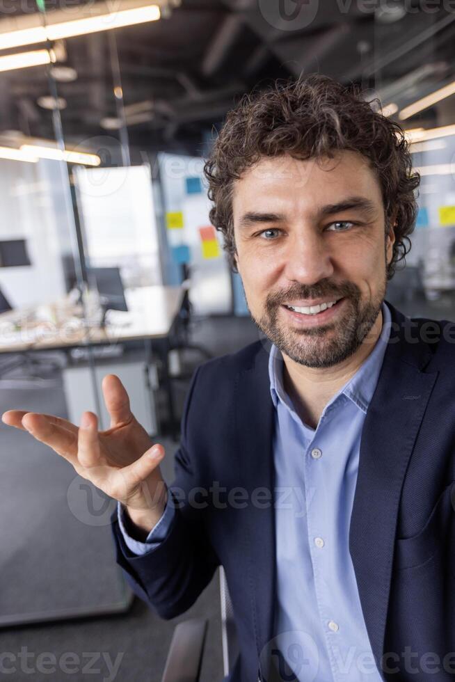 Businessman in modern office engaged in call looking at camera smiling, discussing or presenting. Professional setting with contemporary work environment. photo