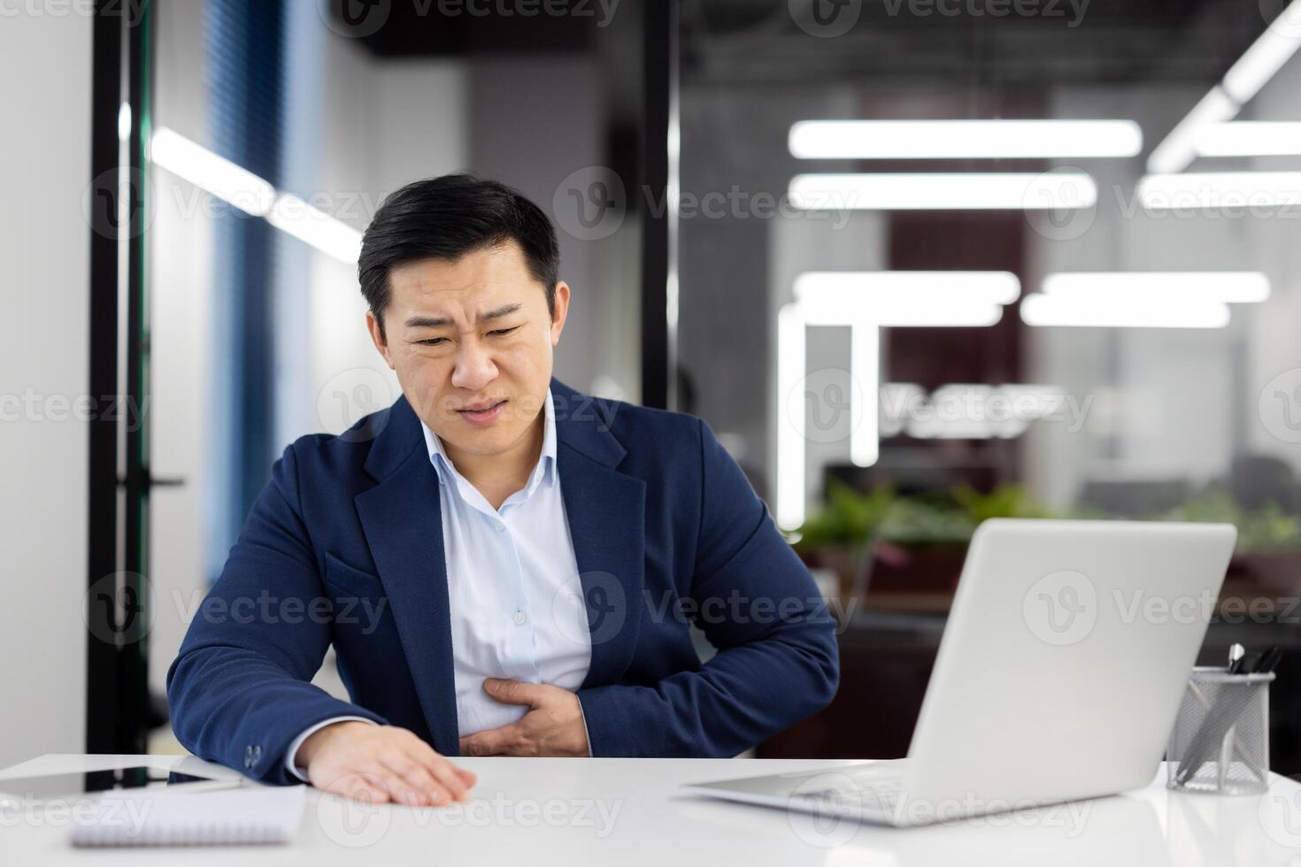 Man has severe stomach pain, nausea and food poisoning, businessman inside office at workplace, worker in business suit working with laptop. photo