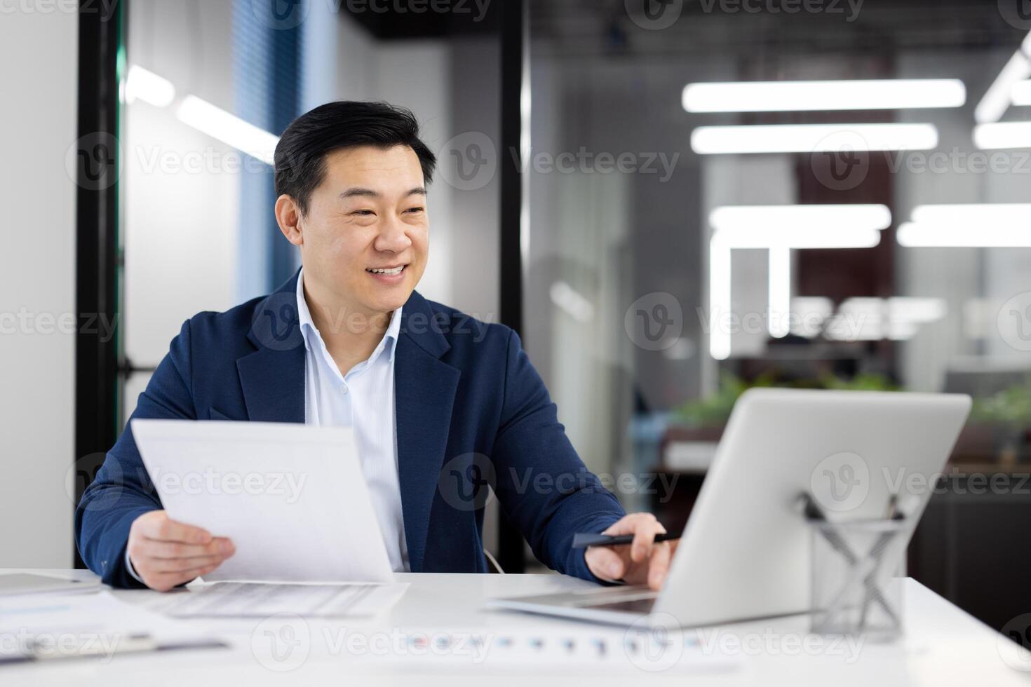 Happy person in formal clothes working by table with pc on background of modern office interior. Busy administrator accomplishing list of daily tasks and sending email with project report. photo