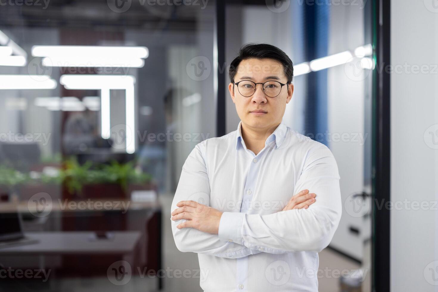 Portrait of serious confident asian man inside office at workplace, businessman in shirt with wrinkled hands and glasses looking at camera, mature boss, financier accountant. photo