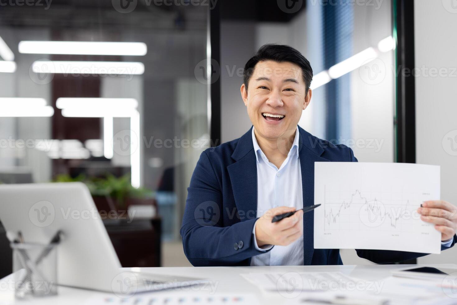 Enthusiastic Asian businessman discussing growth with a financial chart in a modern office setting. He demonstrates success and professionalism. photo