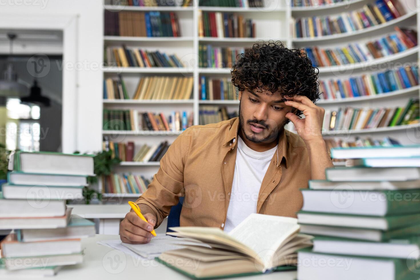 Thinking student preparing for exams inside academic library, man overworked and tired studying alone, hispanic sitting among books doing homework. photo