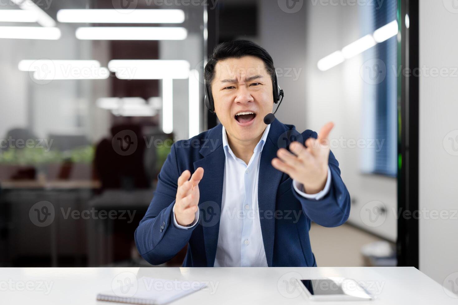 View from laptop camera of handsome asian male shouting in microphone of wireless headset while having online call through modern gadgets. Concept of technology and business. photo