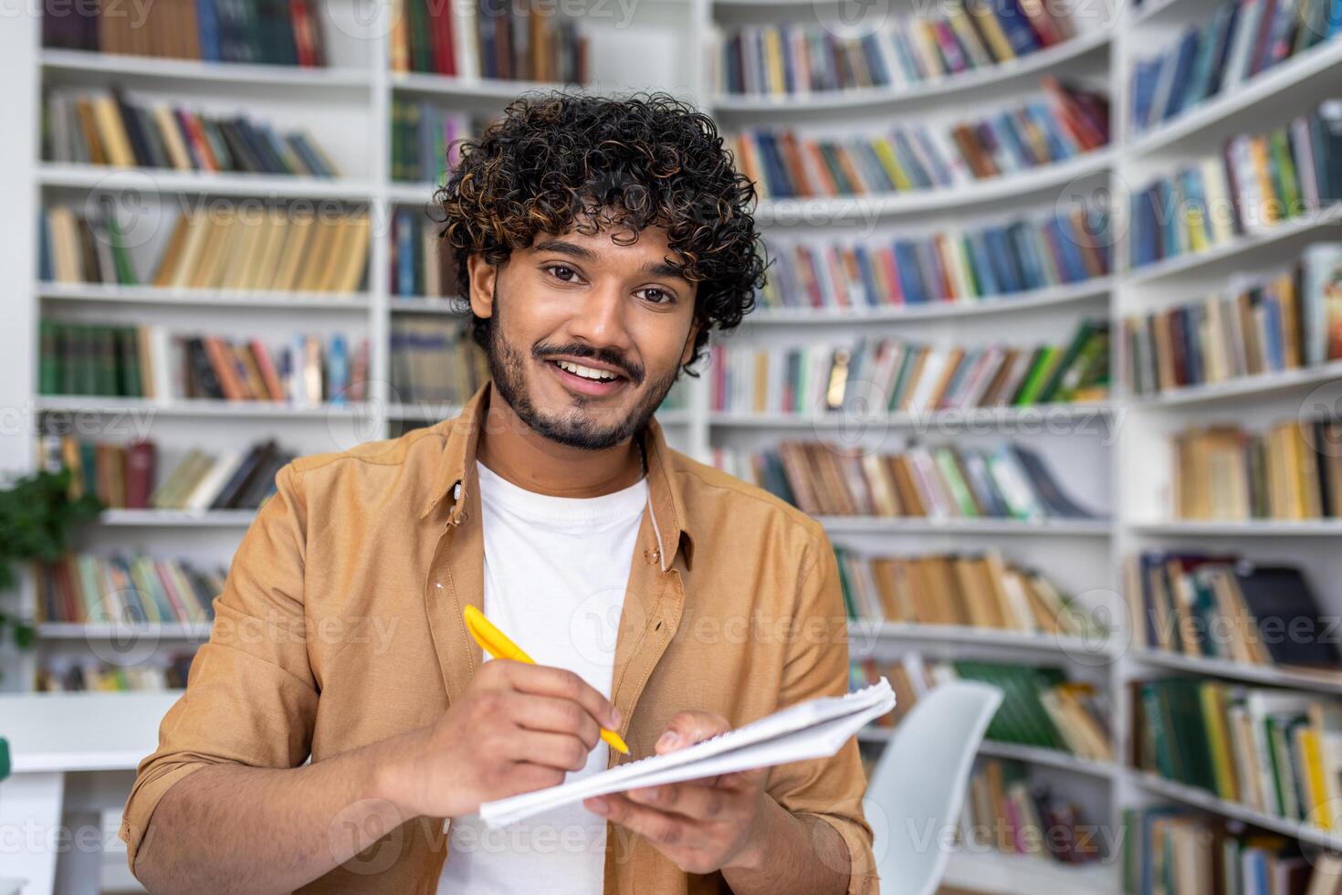 Person in a casual jacket engaged in a call, holding a notebook in a library setting, signaling a learning or educational context. photo