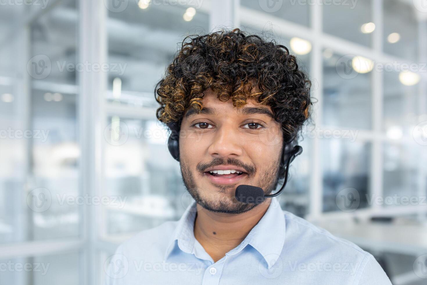 A young professional man smiles while wearing a headset in a brightly lit modern office environment, portraying customer support and professional assistance. photo