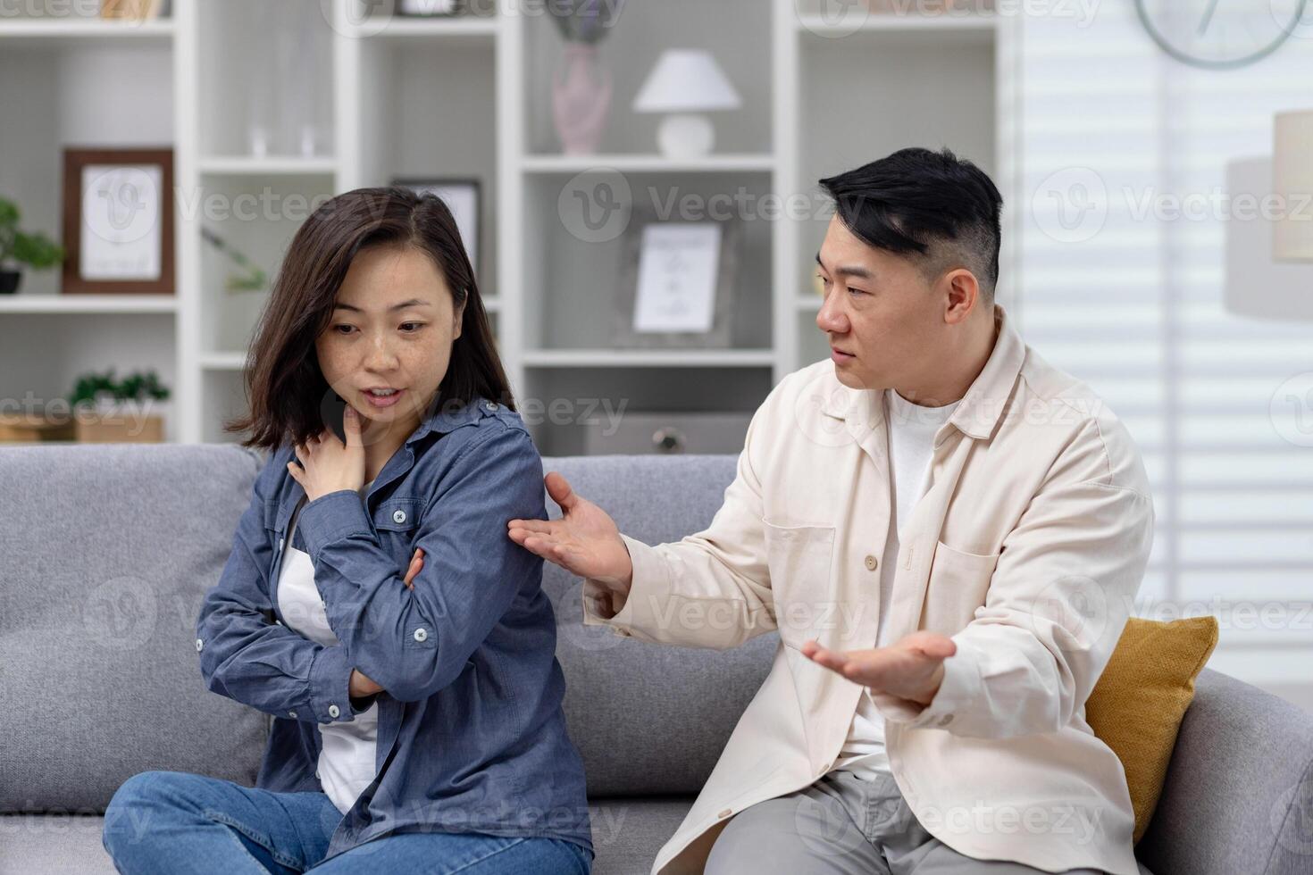 Asian couple having a serious conversation on the couch, capturing emotions of disagreement, concern, and relationship issues in a modern living room setting. photo