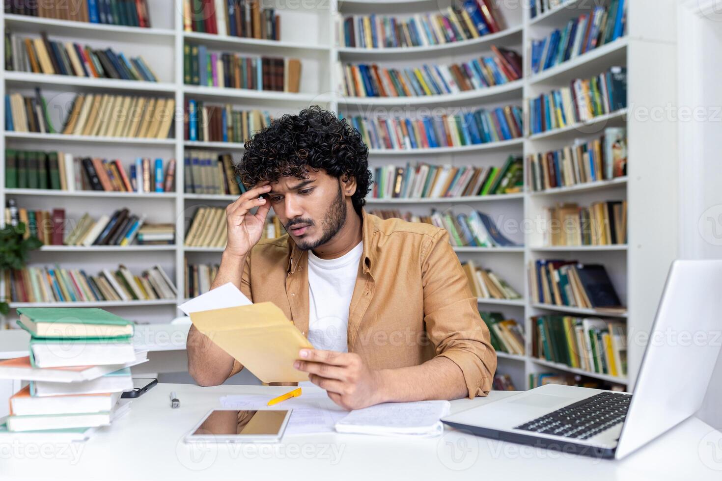 Young hispanic student upset studying inside university campus academic library, disappointed and sad received a letter with bad results in studies and entrance exam. photo