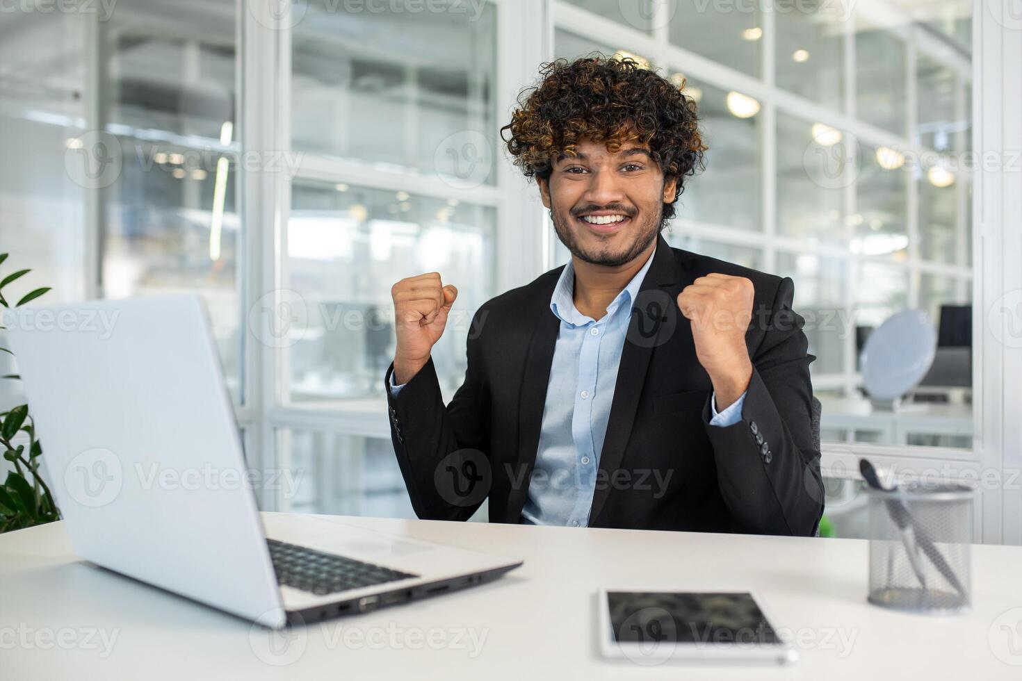 Cheerful businessman celebrating success at his desk in a modern office environment, expressing excitement and positive energy. photo