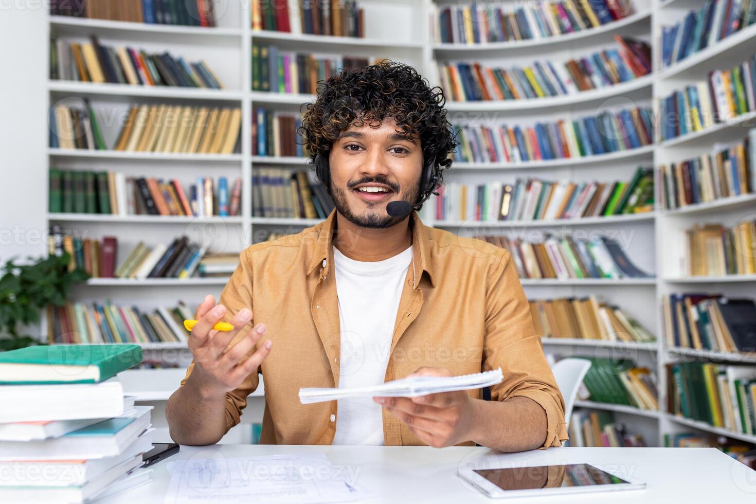 Cheerful young male educator engaging in online teaching using a headset and call technology in a library setting. photo