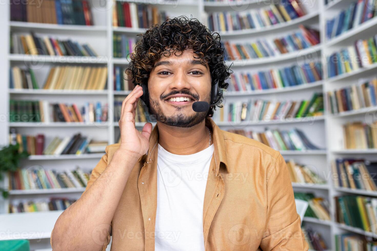A cheerful young man wearing a headset and smiling as he looks at the camera, likely engaging in a call or as a student in a virtual class. photo