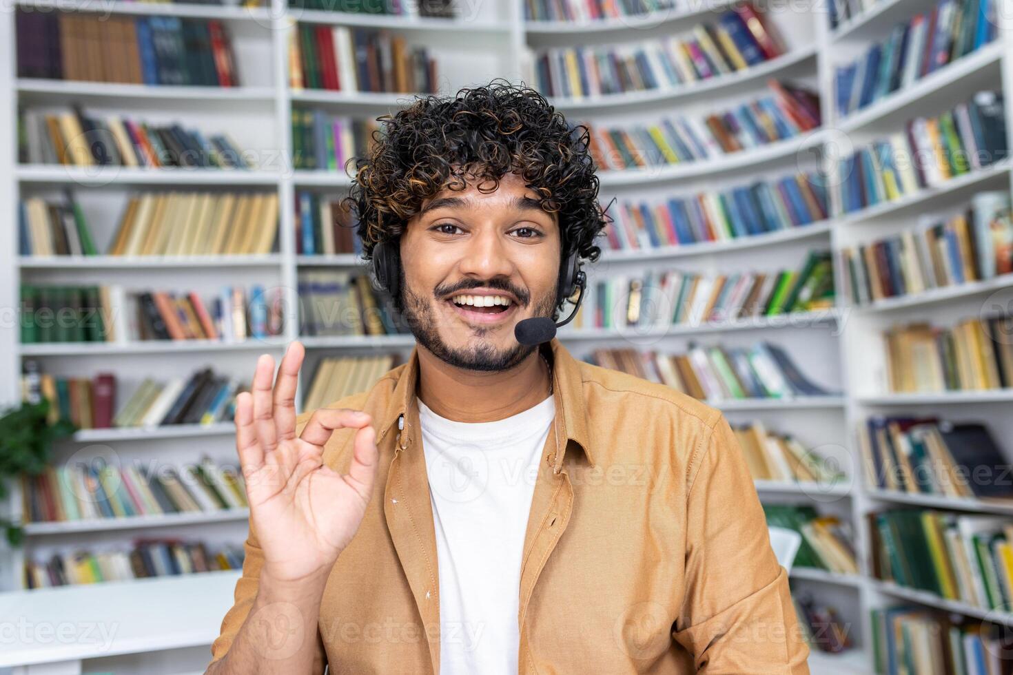 Cheerful student engaging in online learning, making a friendly gesture to the camera while using a headset in a library. photo