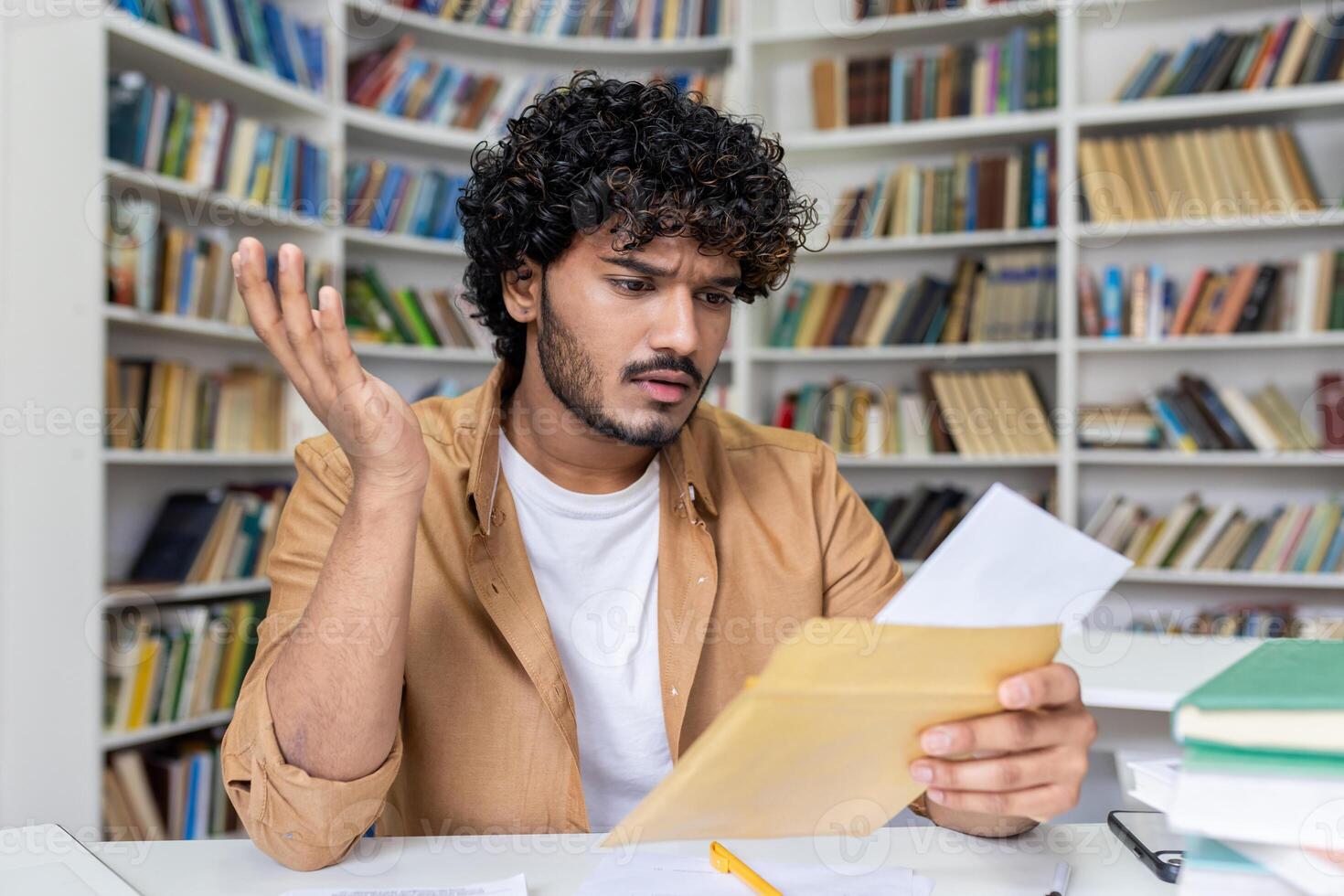 Young hispanic student upset studying inside university campus academic library, disappointed and sad received a letter with bad results in studies and entrance exam. photo