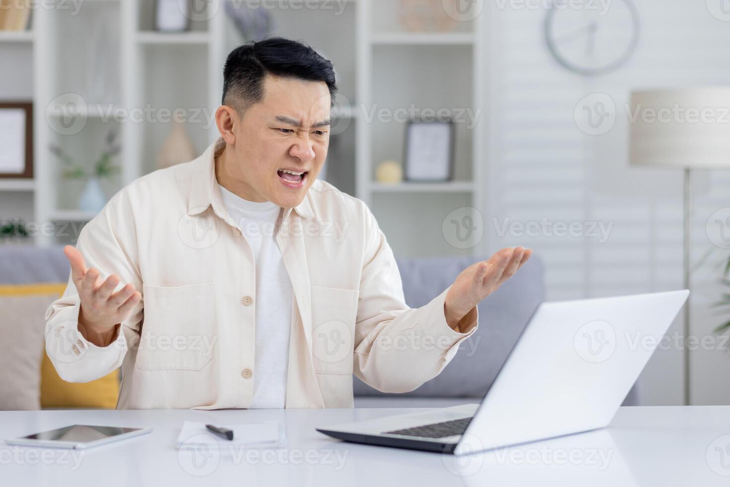 Man showing frustration and anger while looking at laptop in home office setting. Concept of technology issues, work stress, and negative emotions. photo