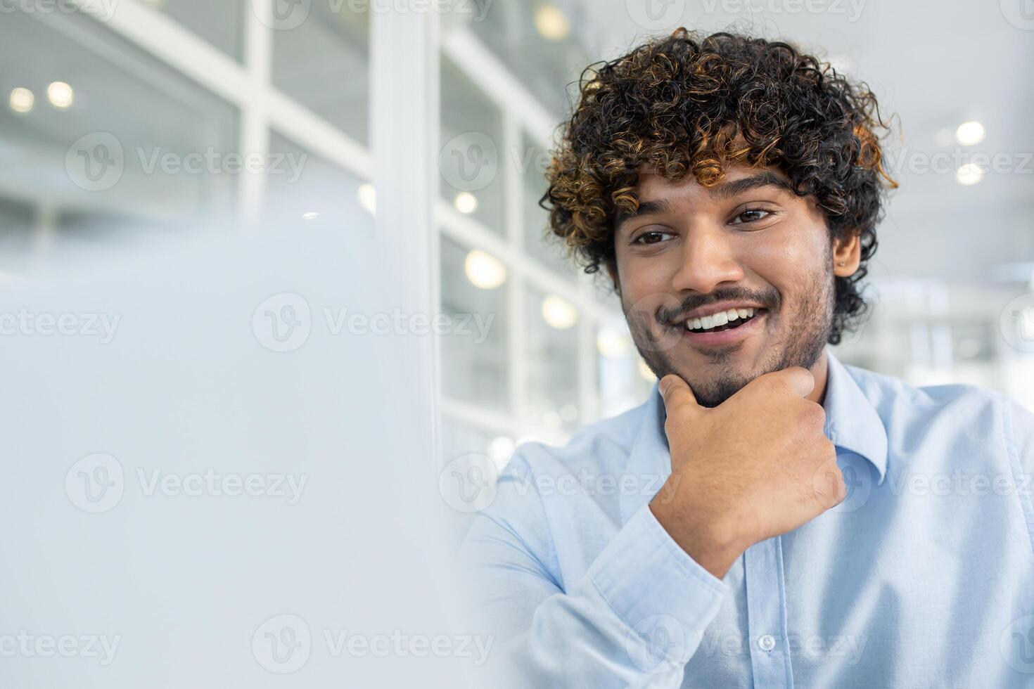 Selective focus on arab trainee holding chin with hand while looking excited at screen of computer. Enthusiastic junior specialist watching webinar and learning new material for work indoors. photo