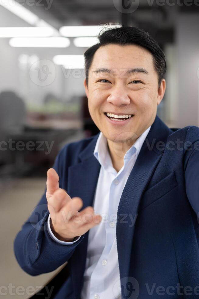 First person view of grown up japanese business person connecting to remote meeting and smiling to camera. Formal man wearing stylish suit while leading call with department of remote workers. photo