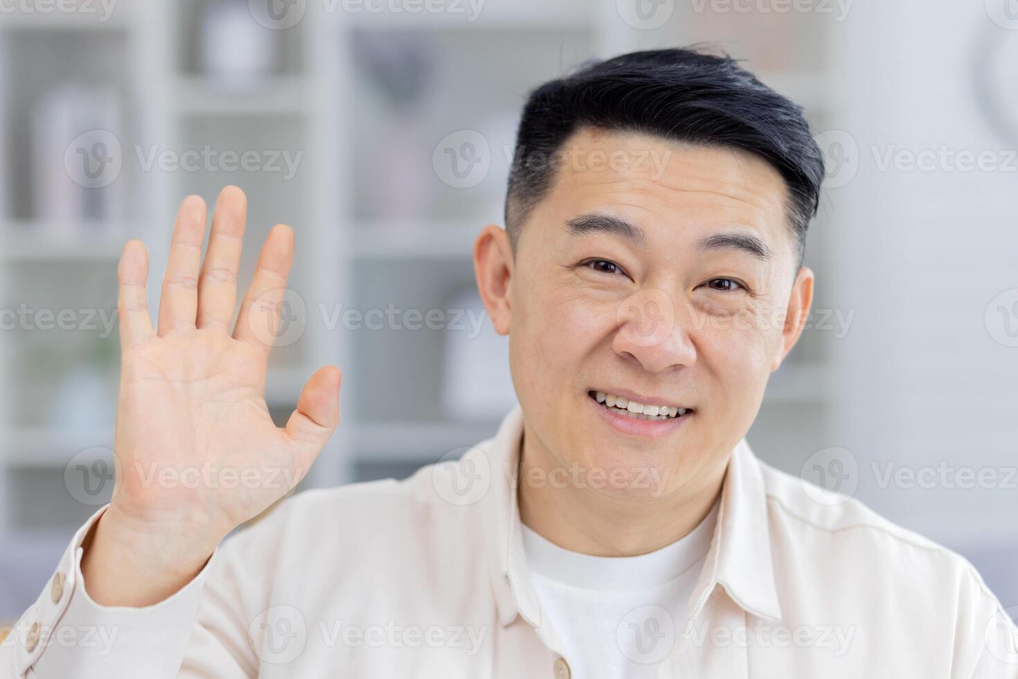 Friendly and cheerful man waving hello with a smile in a casual indoor environment. Perfect for concepts like communication, greeting, or friendship. photo