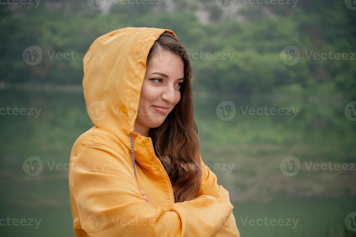 A woman in a yellow raincoat is standing in front of a body of water photo