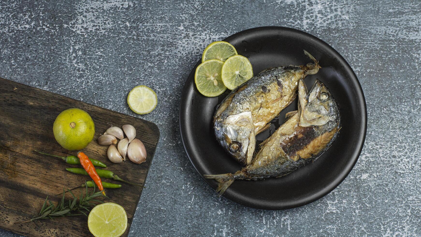 two short mackerel fish on a plate with lemon slices and garlic photo