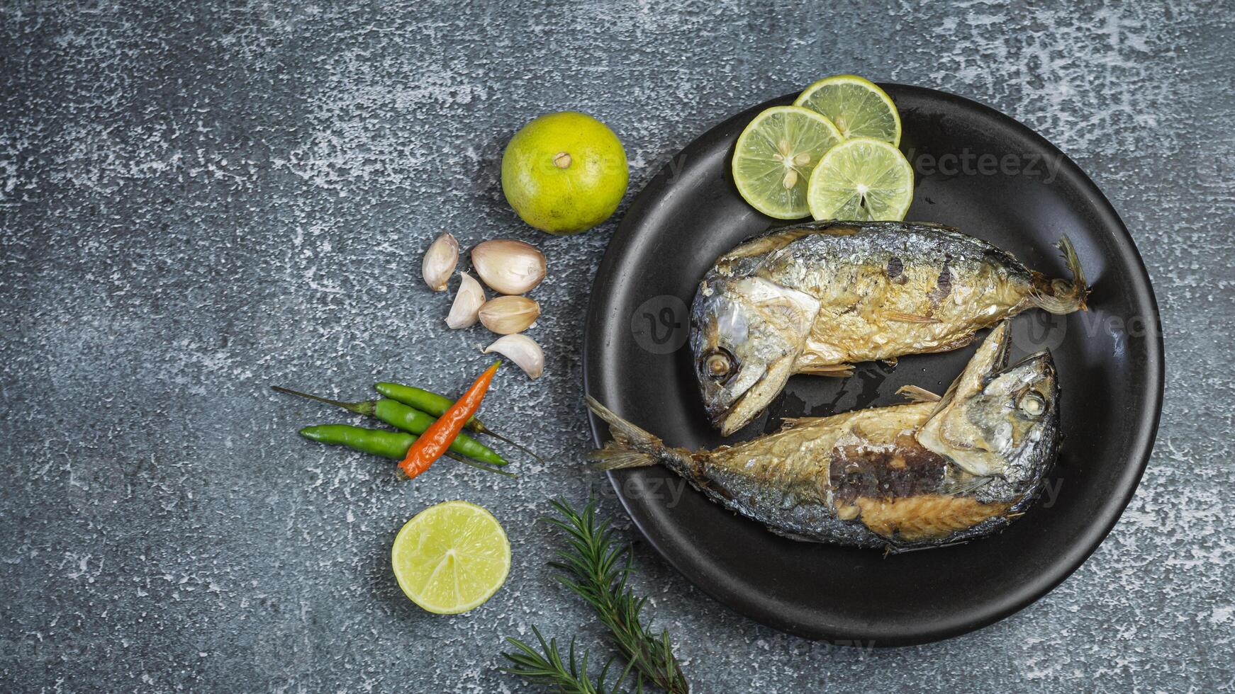 Short mackerel grilled on a black plate with lime and herbs photo