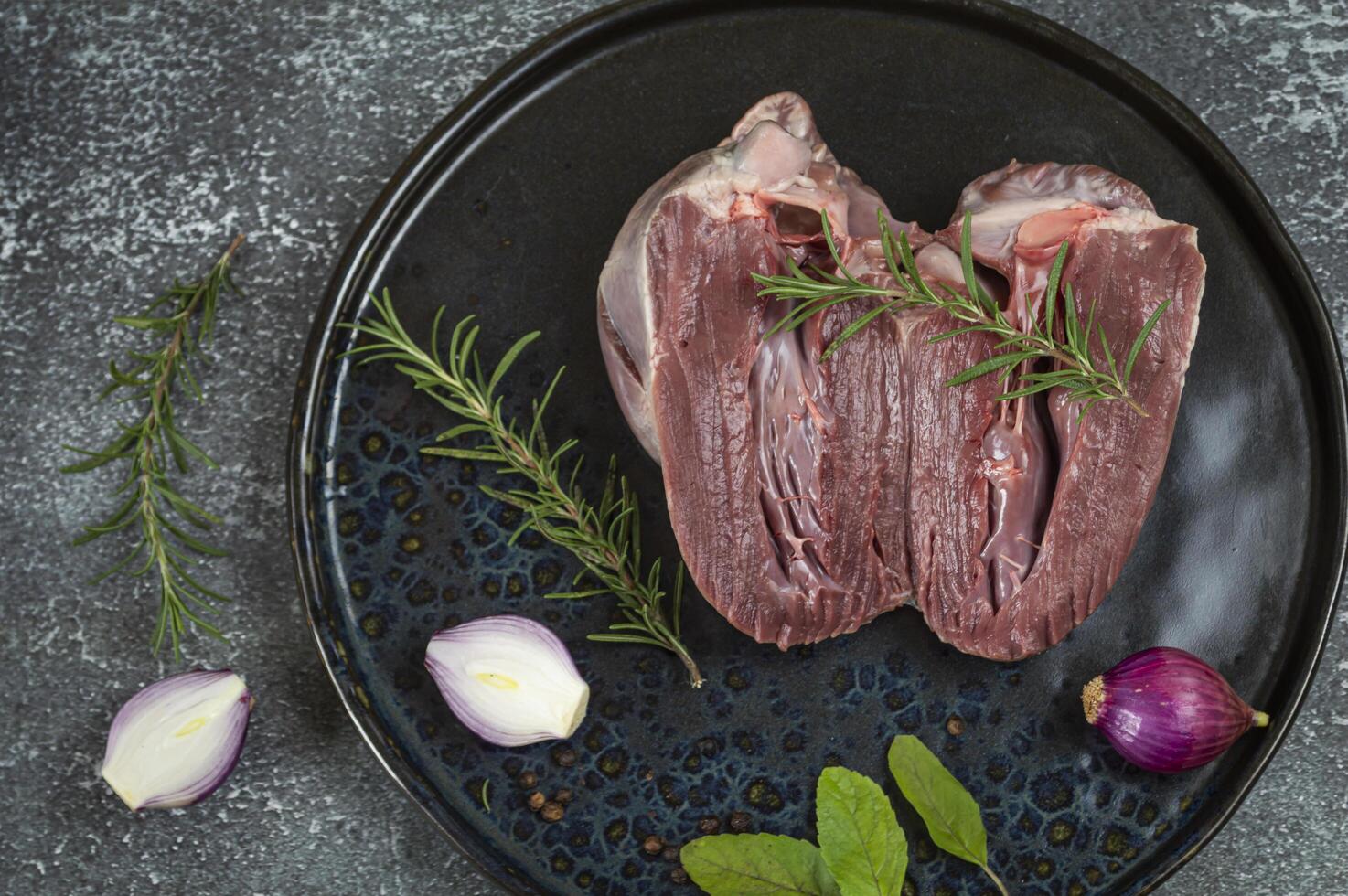 raw pig heart on a black plate with herbs and onions photo