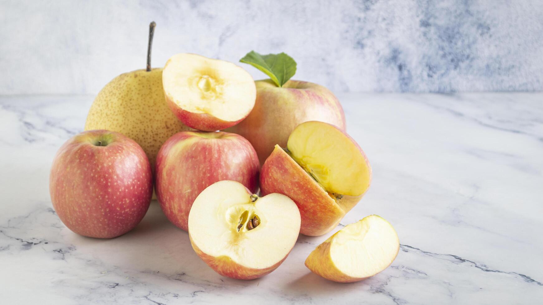 a pile of apples and a pear on a marble surface photo