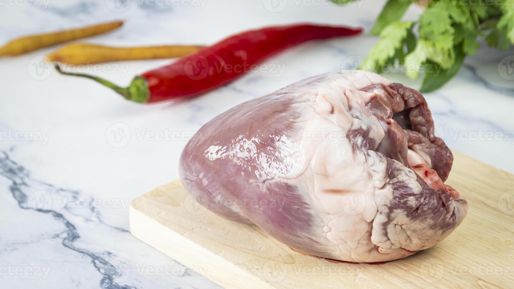 a raw pig heart on a cutting board with a pepper and other vegetables photo