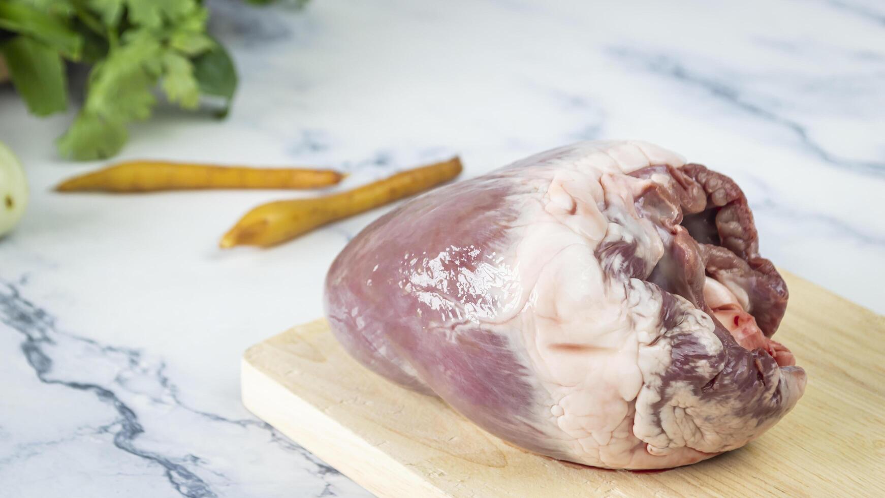 a raw pig heart on a cutting board with vegetables photo