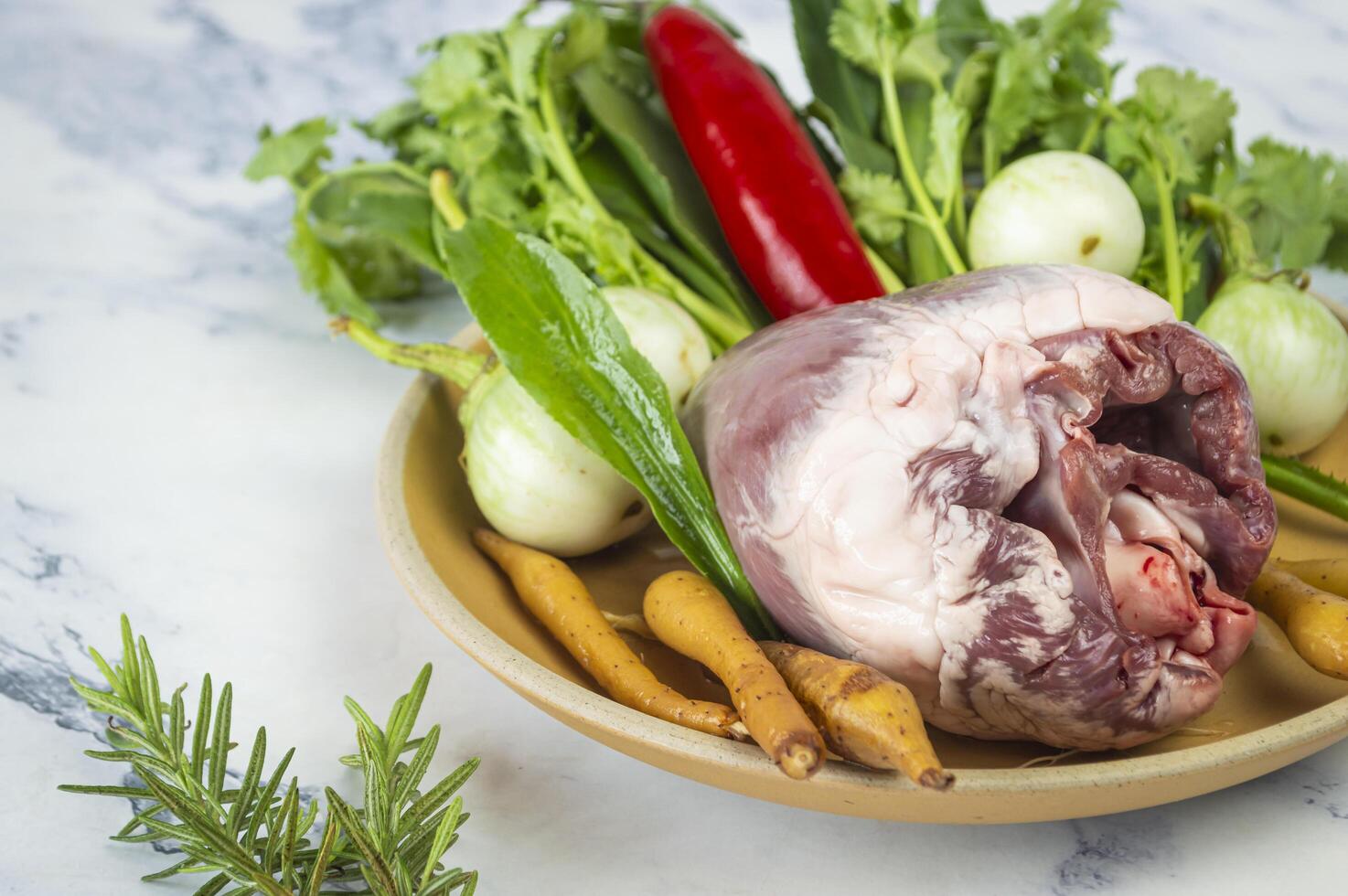 a bowl of raw pig heart meat, vegetables and herbs on a marble counter photo