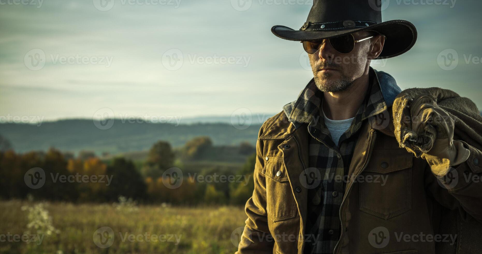Man in Cowboy Hat and Jacket Walking Through Field photo