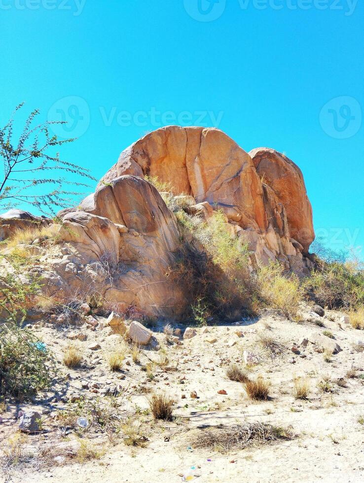 a large rock in the desert with a blue sky photo