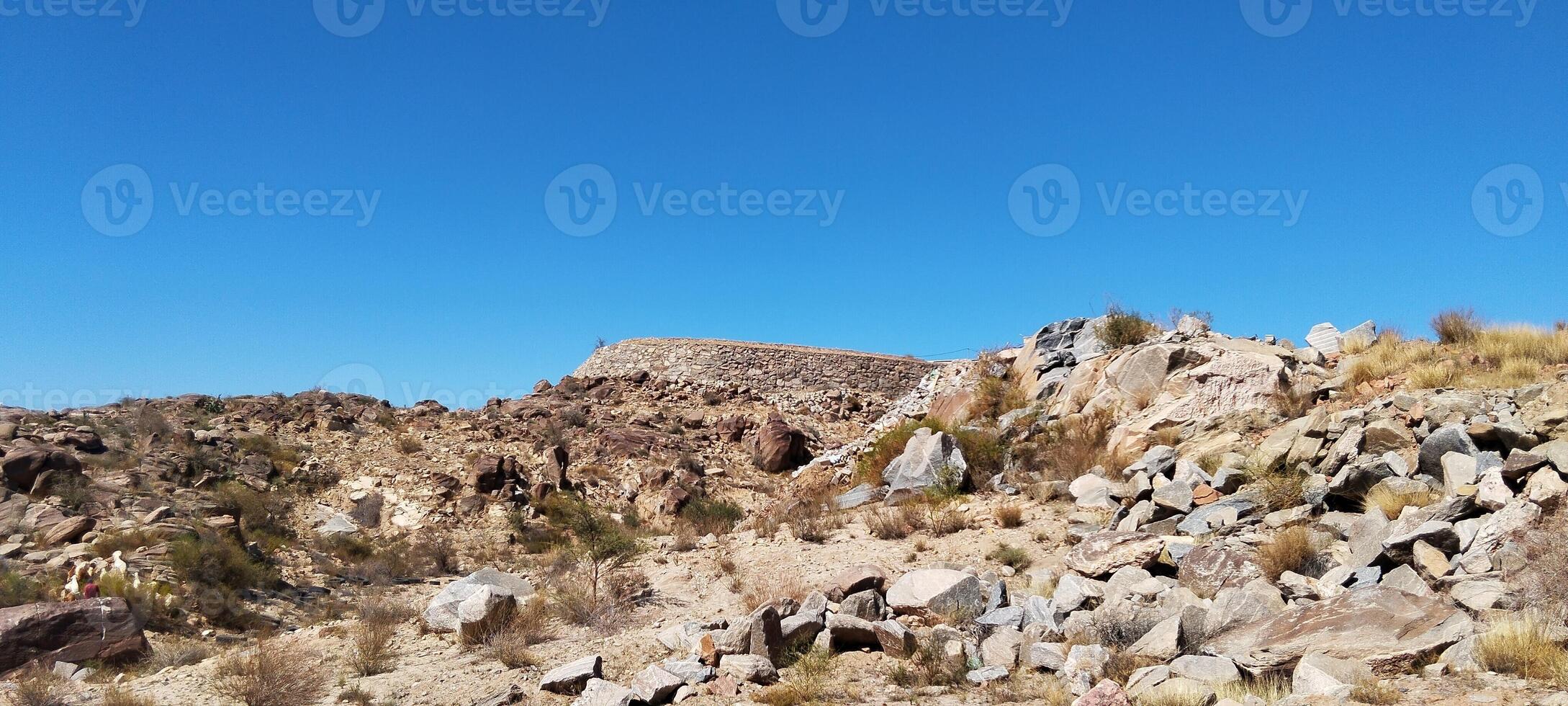a rocky hill with rocks and bushes in the desert photo