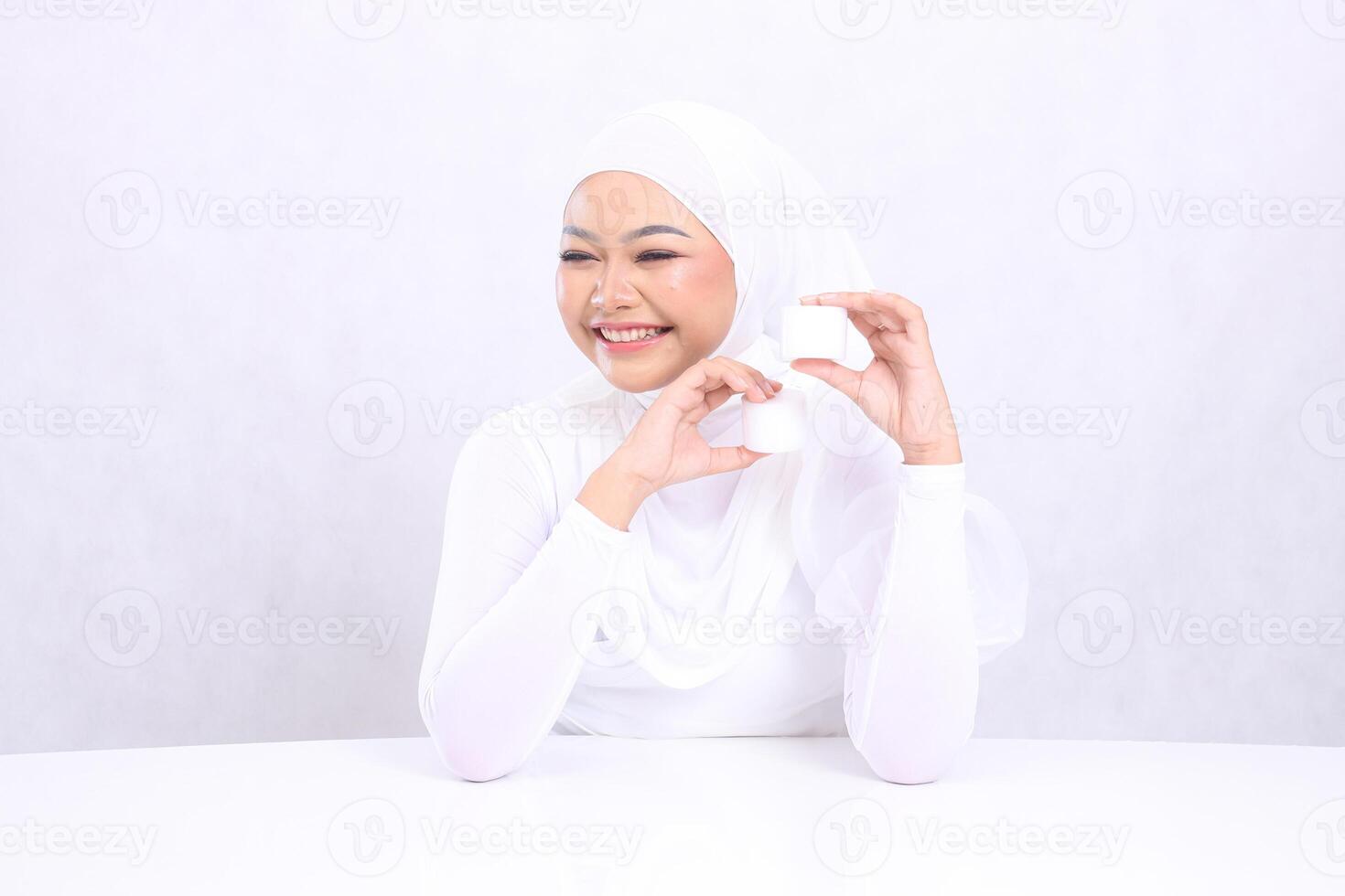 Gesture Beautiful young hijab woman asia happy to the front both hands holding cosmetic cream top and bottom for daily skin care routine needs on white background. Facial treatment, Perfect skin photo