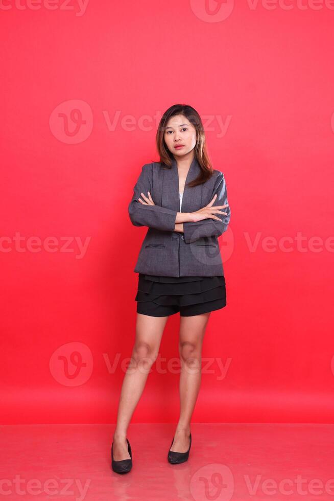 Cool asian female executive in gray suit with long hair, white skin, taking photo in studio with red background standing with her arms crossed. for corporate concepts, fashion and advertising