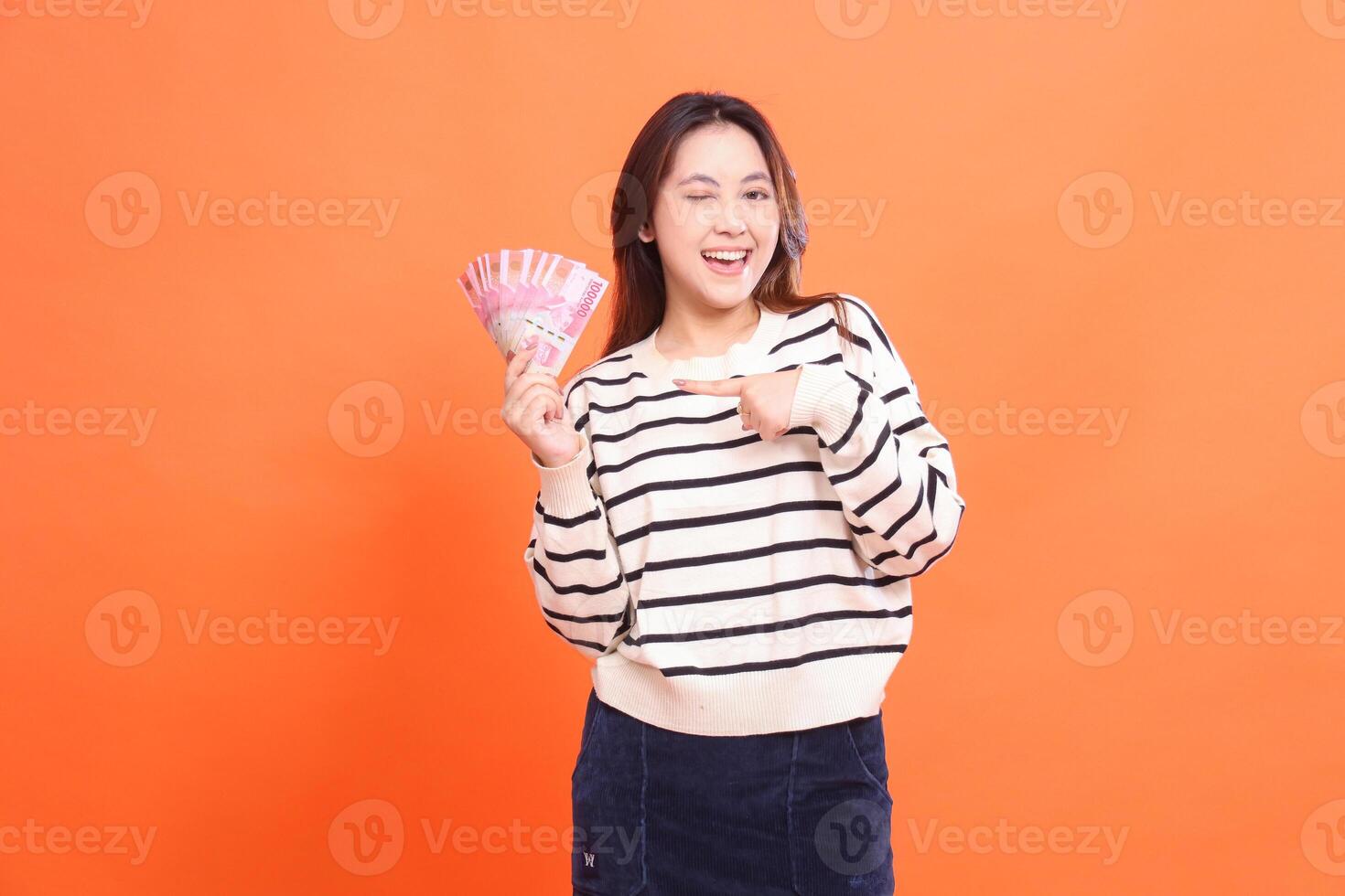 The expression of a cheerful Asian woman winks standing while holding some rupiah money for doing business. for fashion, business and finance concept photo