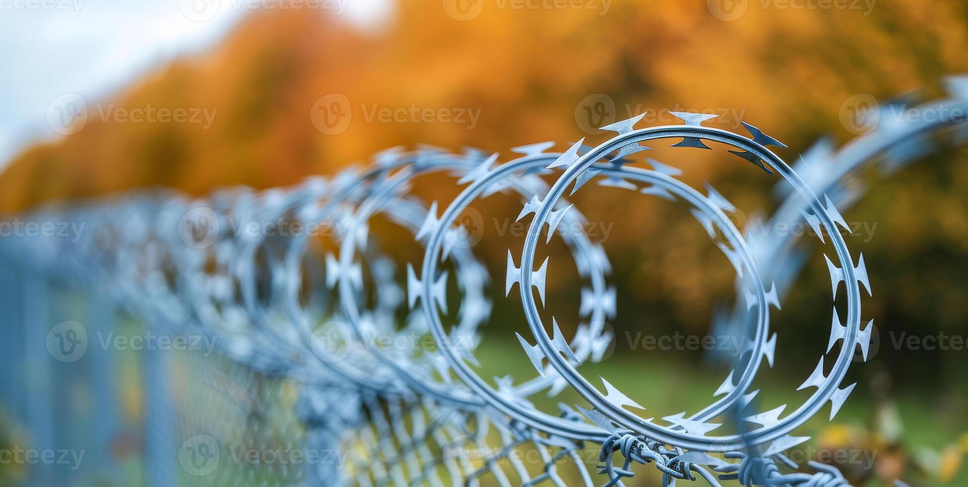 A fence with barbed wire on top of it. The fence is on the side of a road, and there are trees in the background photo