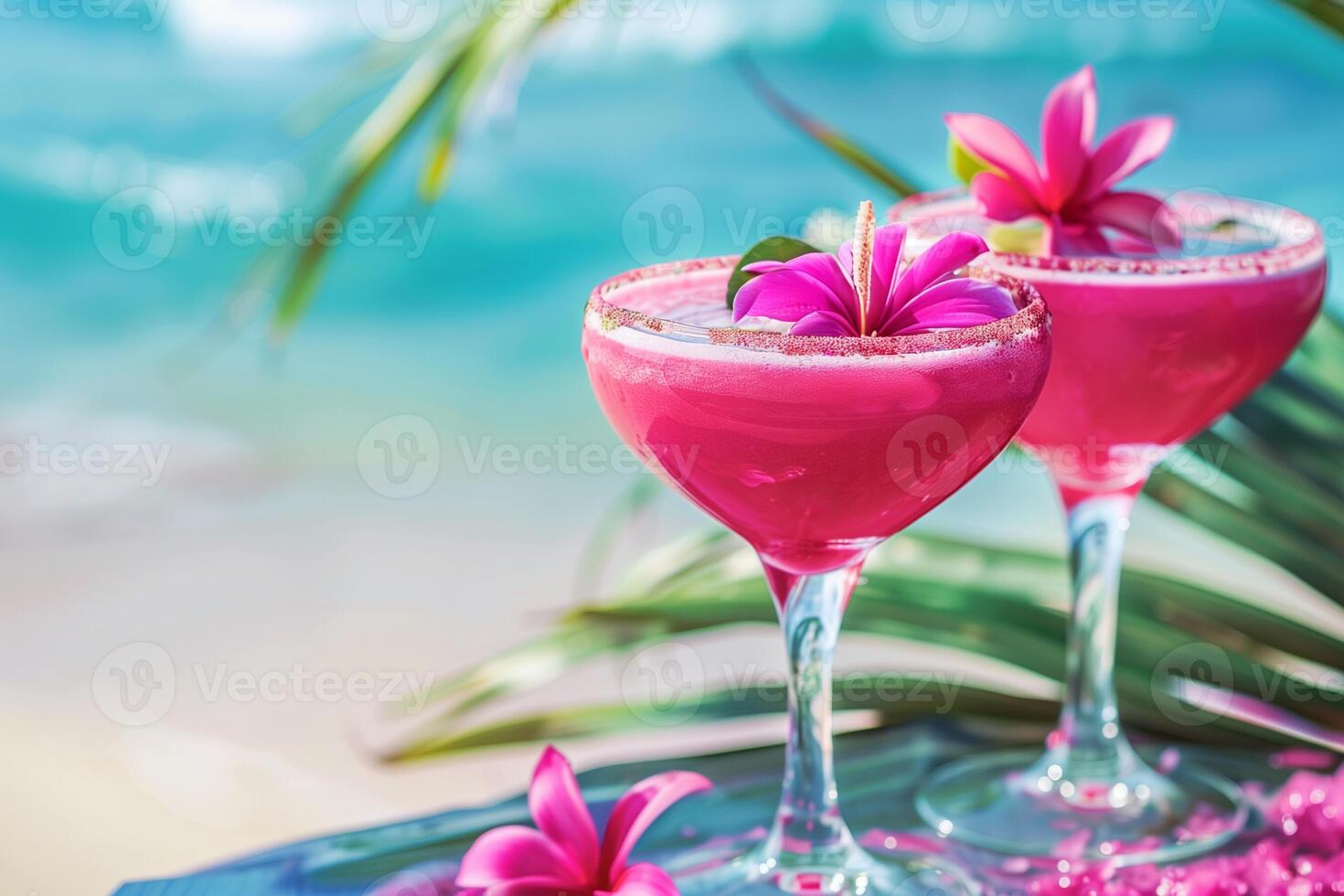 Tropical pink cocktails in glass flutes with tropical flowers against a vibrant blue ocean backdrop photo