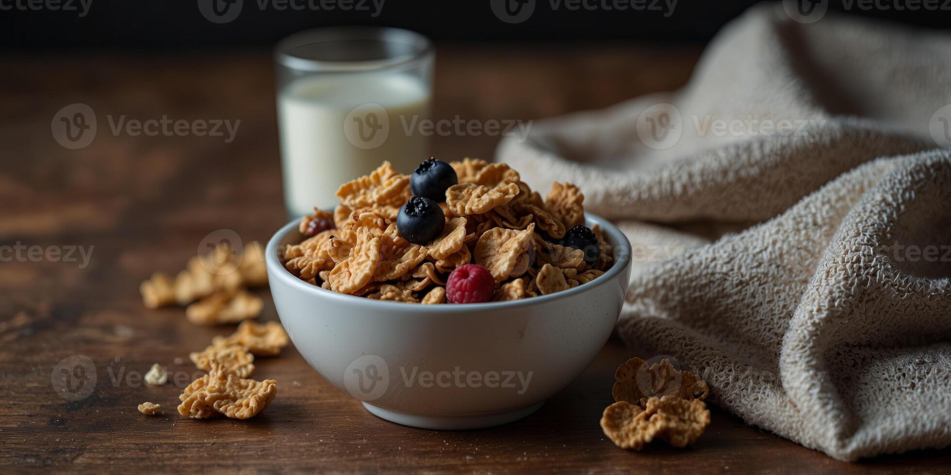 On a wooden surface there is a spread with a bowl of cornflakes dried berries granola bar and a glass of milk on a towel with empty space in the image with copy space image. photo