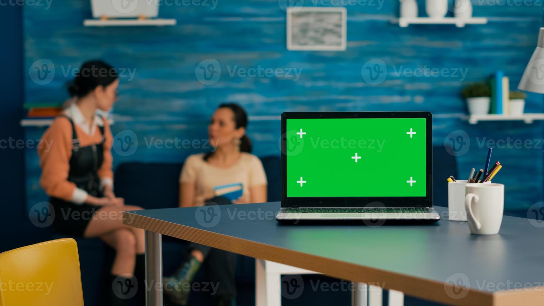 Laptop computer with mock up green screen chroma key standing on desk while in background two women talking about business commerce. Home studio is eqquiped with powerful isolated pc photo