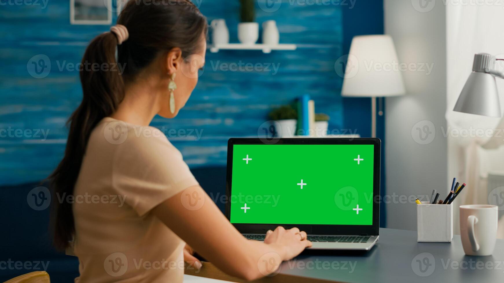 Back shot of freelencer working at marketing project using isolated pc with mock up green screen chroma key display. Woman typing on laptop computer sitting in home office studio photo