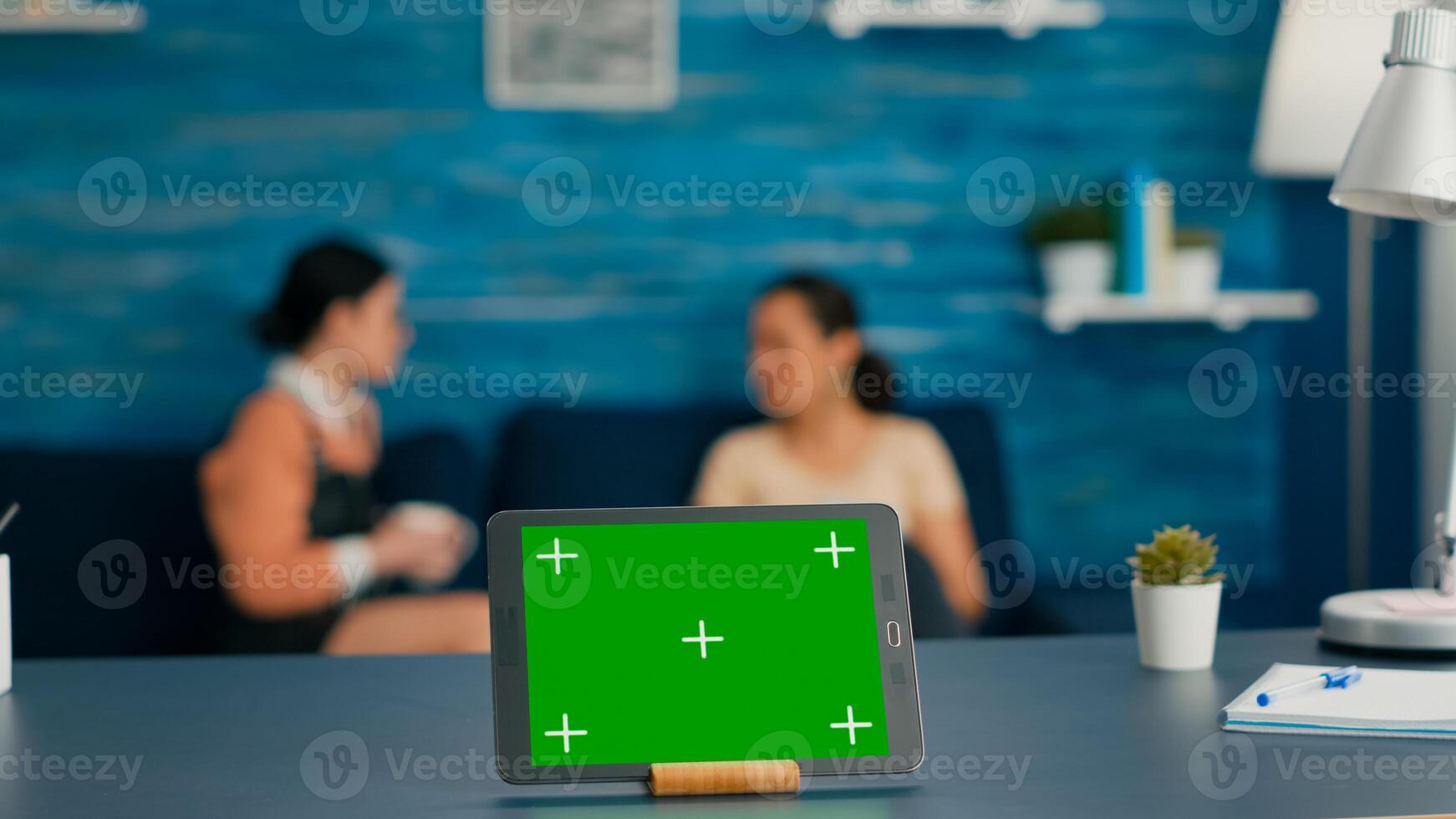 Isolated digital tablet with mock up green screen chroma key display standing on office desk in living room. In background room collegues talking about online communication photo